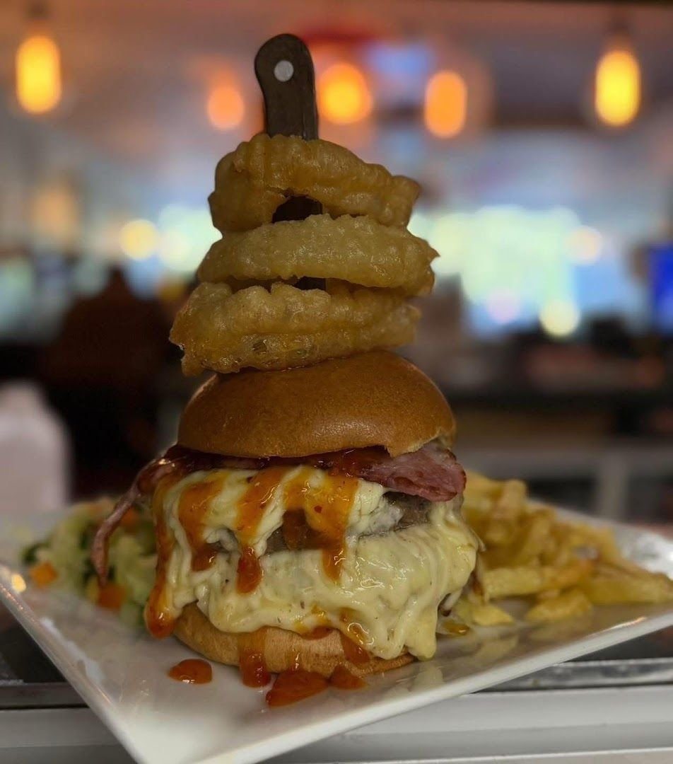 A burger stacked with cheese and a tower of onion rings on a skewer, with chips